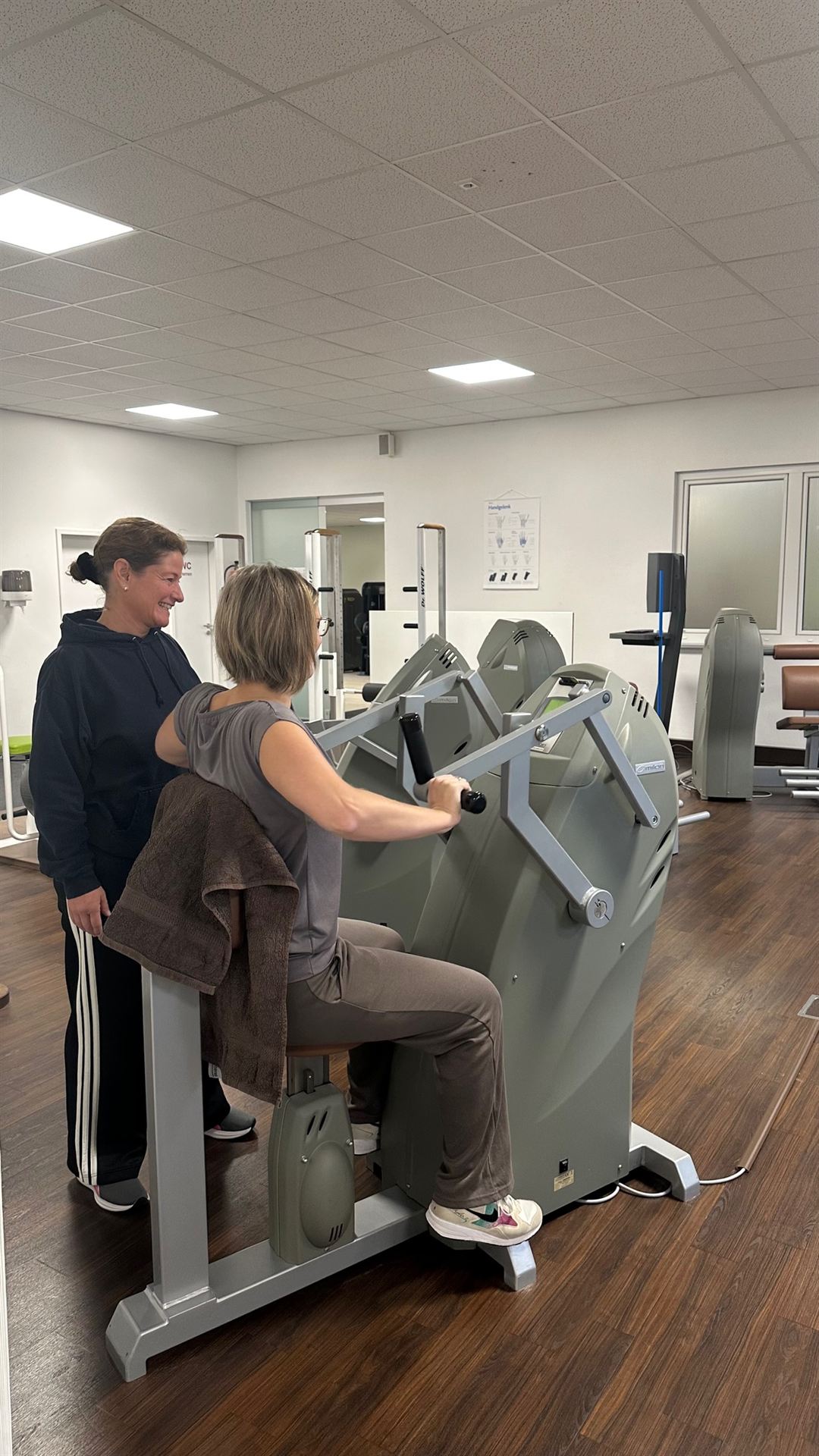 Physiotherapeutin begleitet lächelnd eine Patientin am Milon-Trainingsgerät